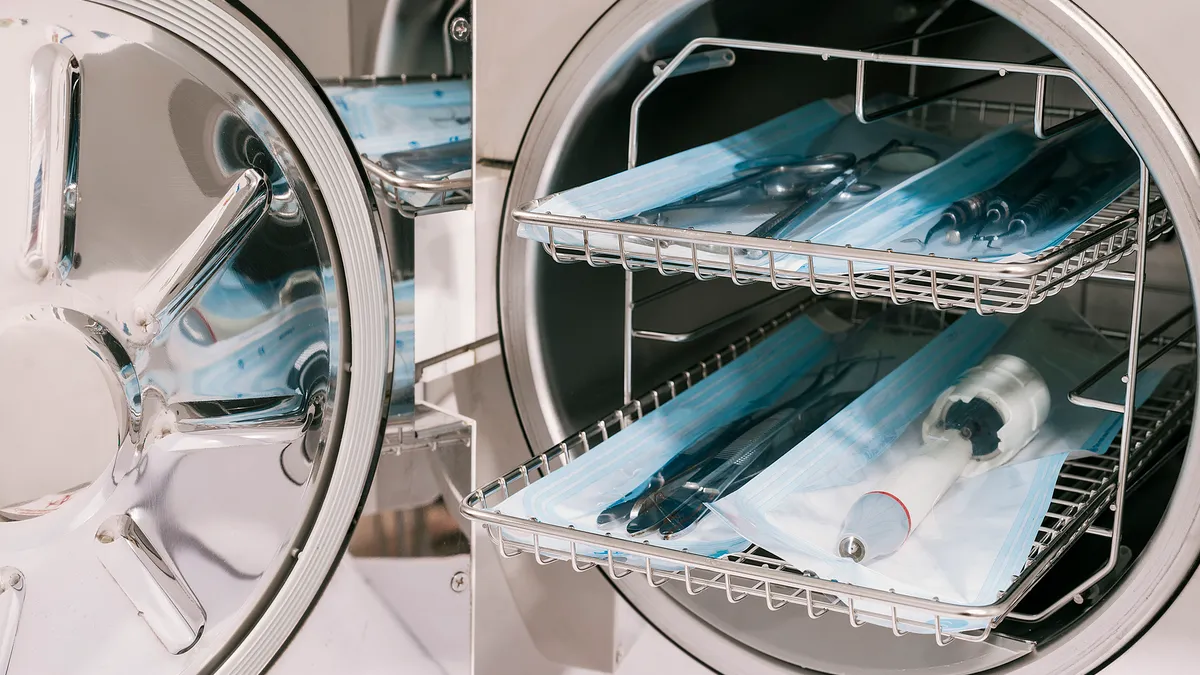 Dental tools and masks sit inside a two trays in a machine, with the door open.