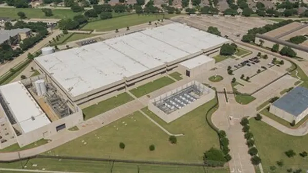 A large building is situated amid green space and parking lots on a bright day.