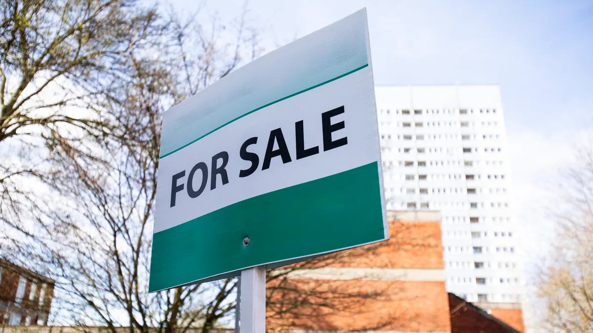 For sale sign with apartment building in the background