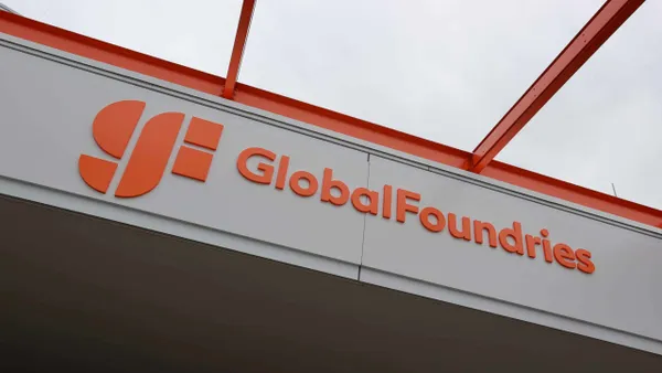 The orange GlobalFoundries logo on a wall near a lit ceiling.