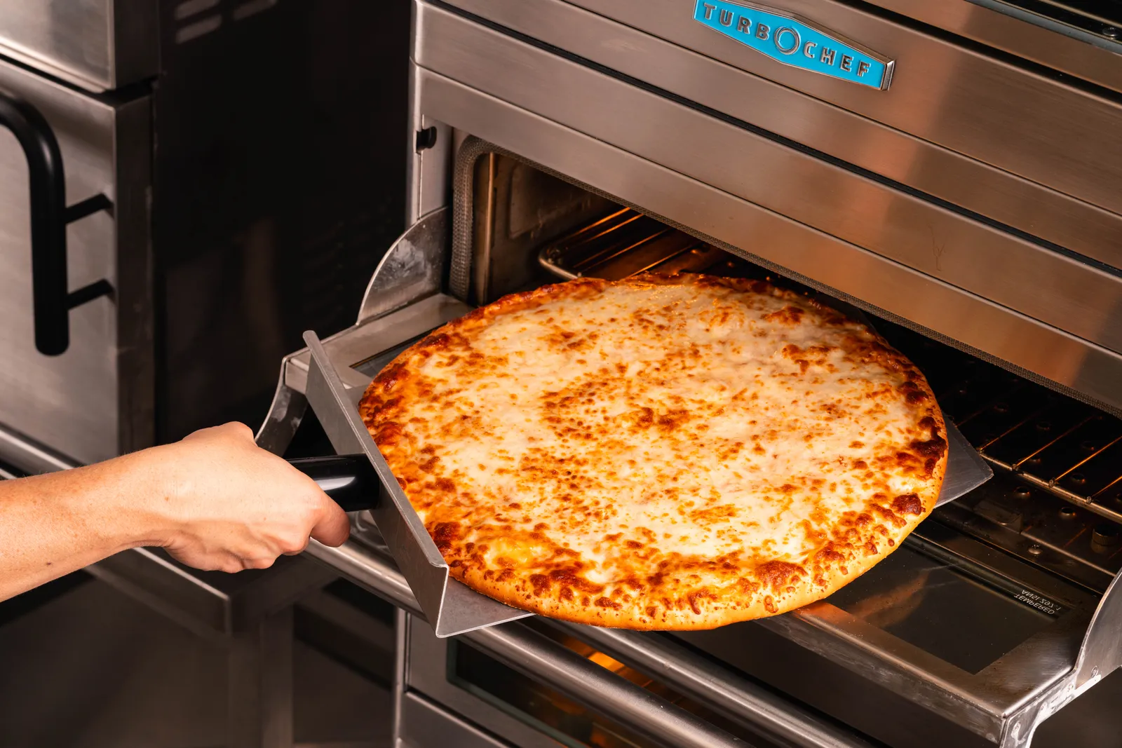 A photo of a cheese pizza from McLane Company's Prendisimo line being put into a pizza oven.