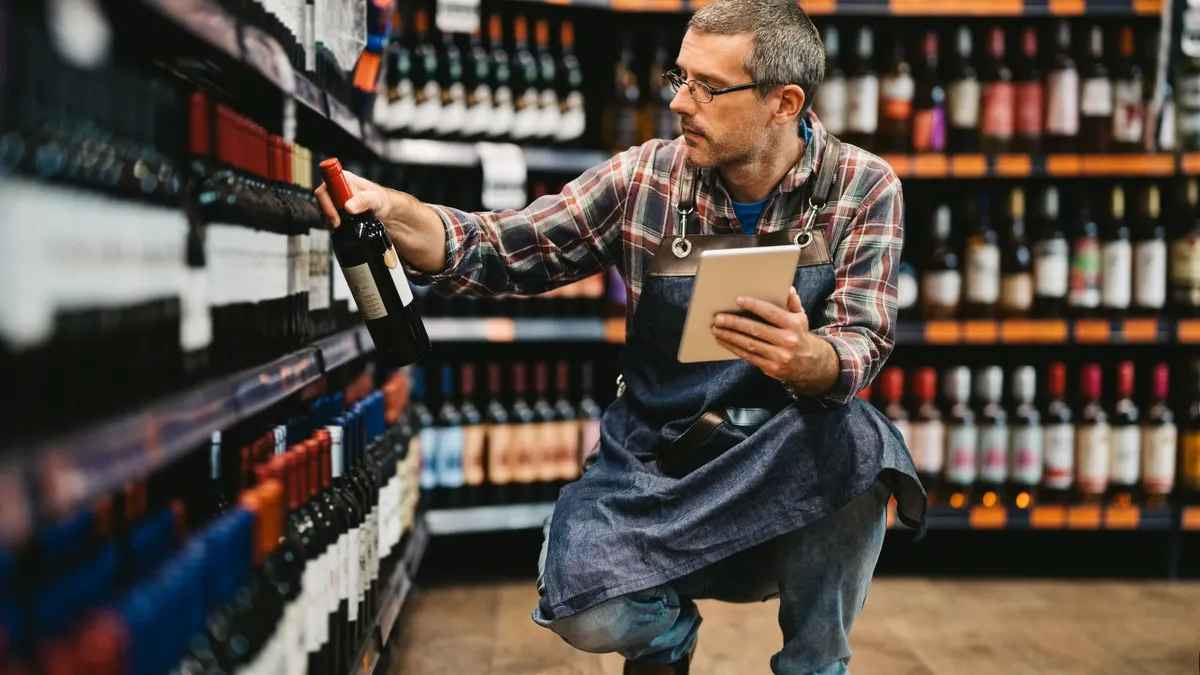 A person squatting in front of shelves of wine bottles.