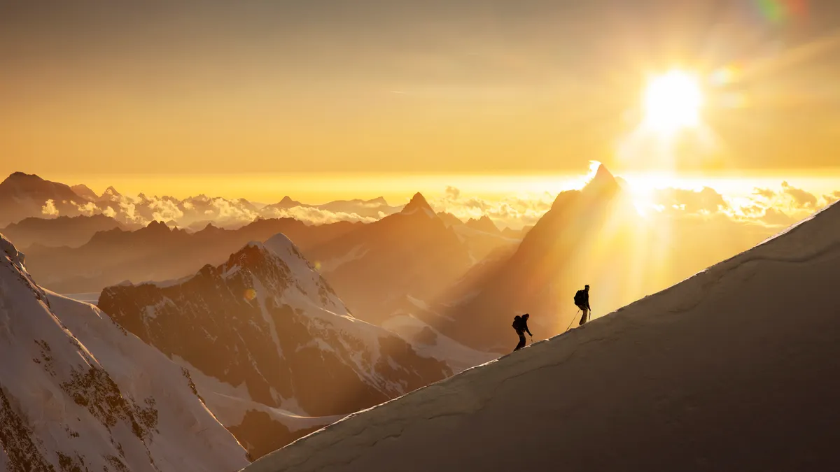 Two hikers climbing up a snow mountain during sunrise