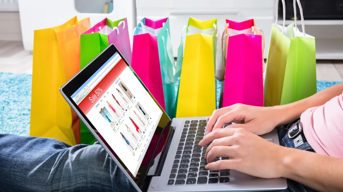 Woman Sitting On Carpet Using Laptop To Shop Online Besides Colorful Shopping Bags