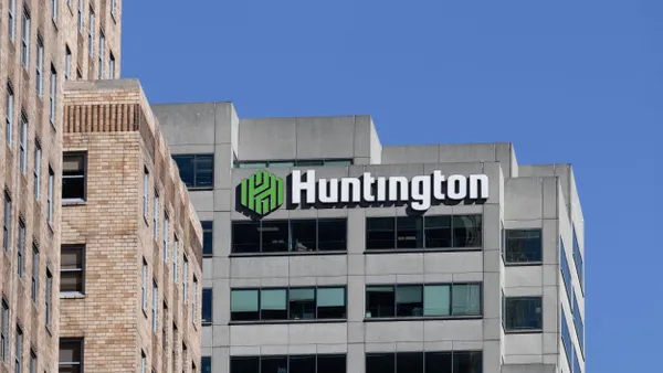 The building features the bank's distinctive green and white signage, with large glass windows and a brick façade with a clear blue sky behind it. 