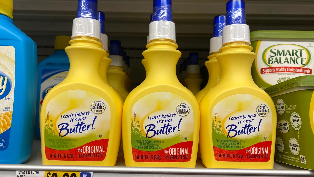 Bottles of I Can't Believe It's Not Butter Spray sit on a grocery store shelf next to other buttery spreads.