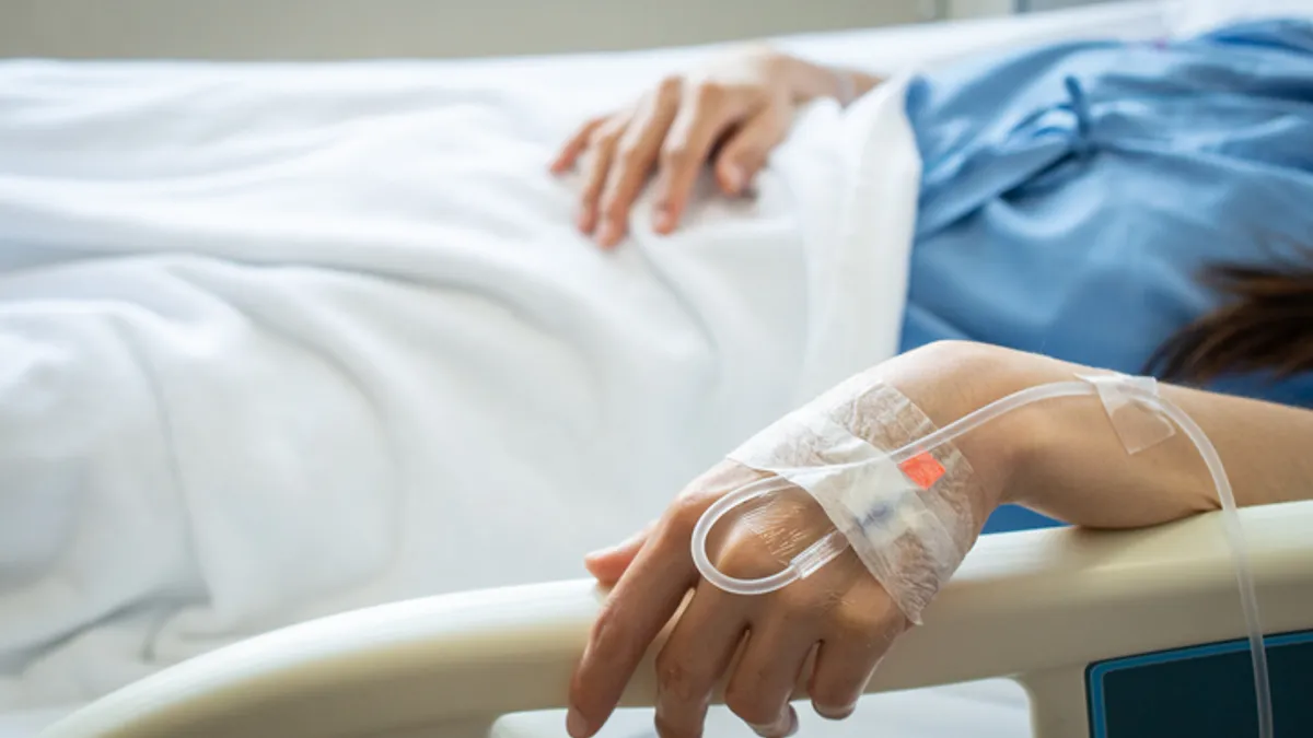 A hospital patient receives medication through an IV in their hand.