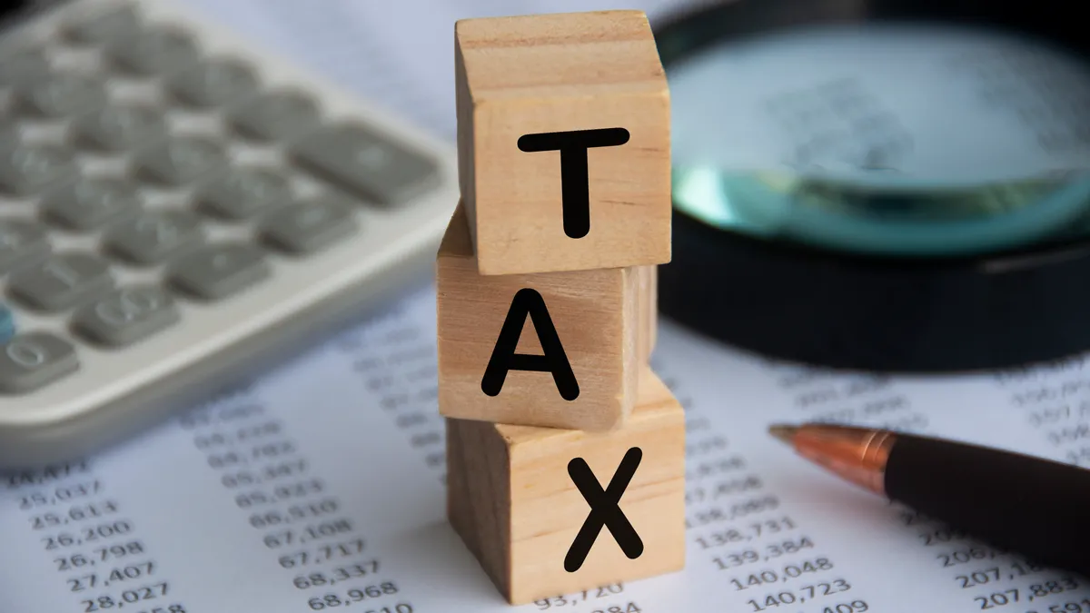 Tax word on wooden blocks with calculator, pen, magnifying glass and data analysis background.