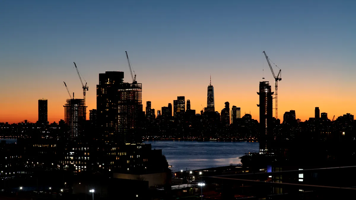 Construction cranes line the city skyline at dusk in New York City.