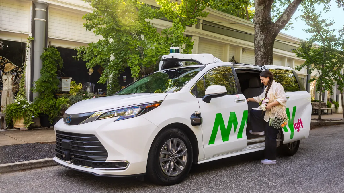 A woman is about to enter a white minivan labeled "May Mobility" and "Lyft."