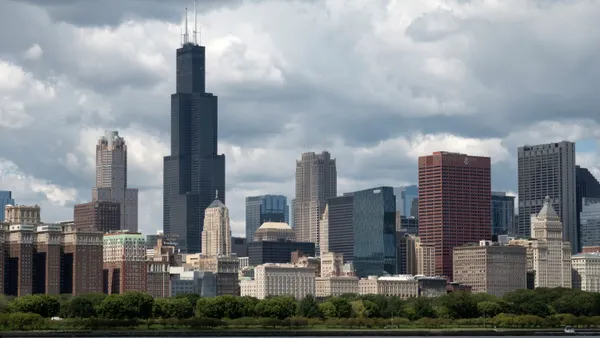Skyscrapers are seen against a cloudy sky, with water in the foreground.