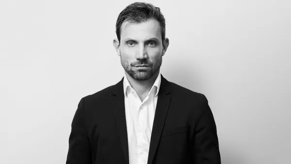 Black-and white headshot of a man wearing a suit without a tie, staring at the camera.