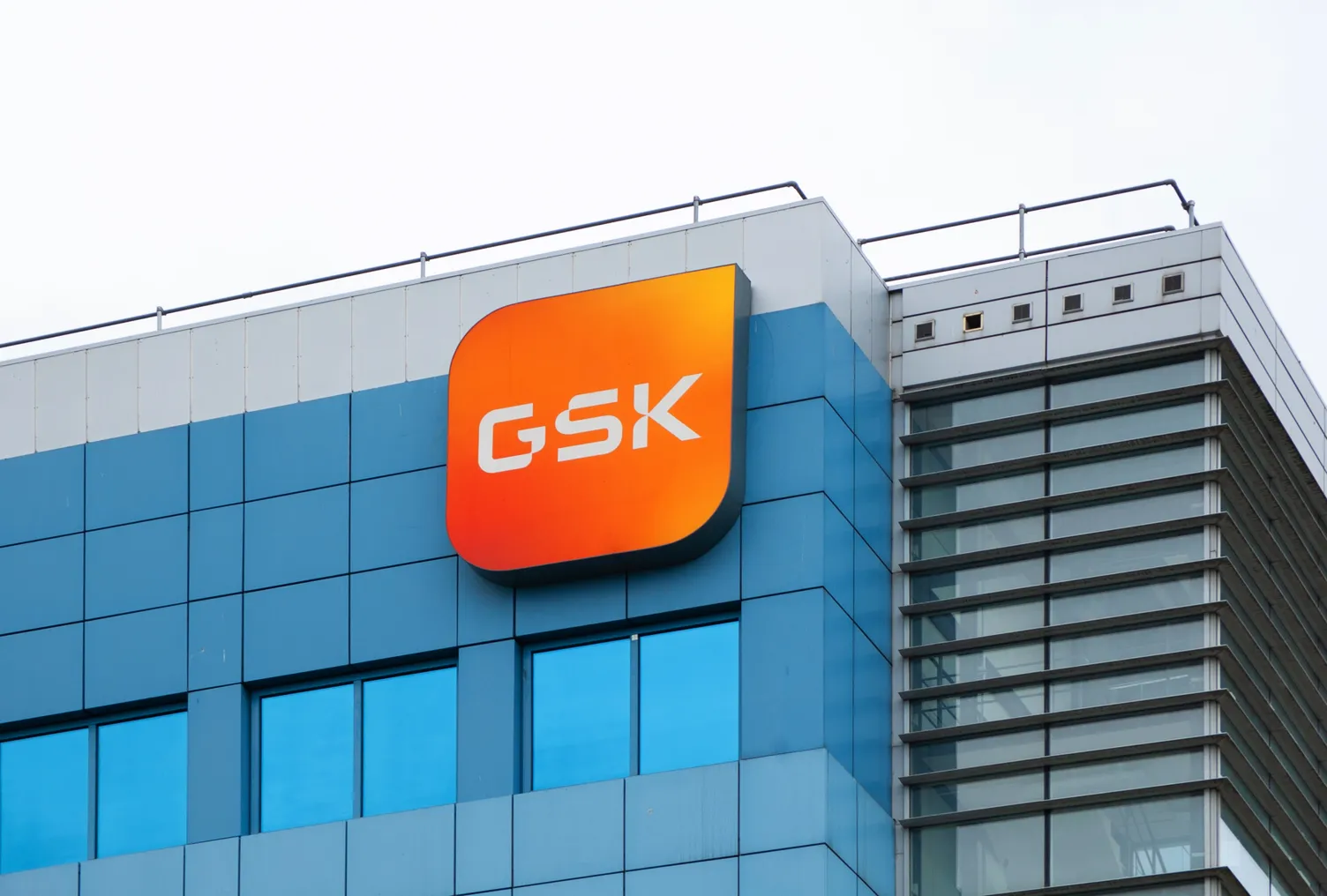 A sign with the letters GSK hangs on the side of an office building.