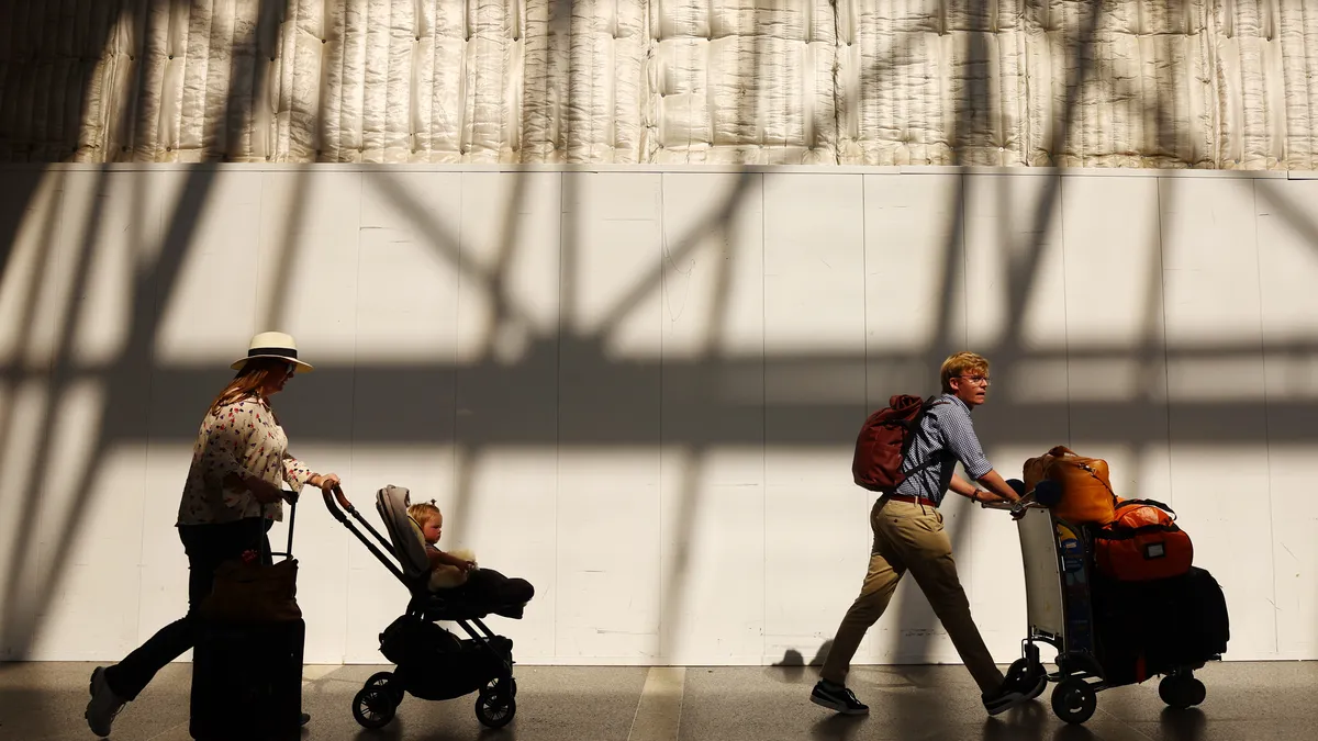 A person pushes a stroller and another person pushes a luggage cart.