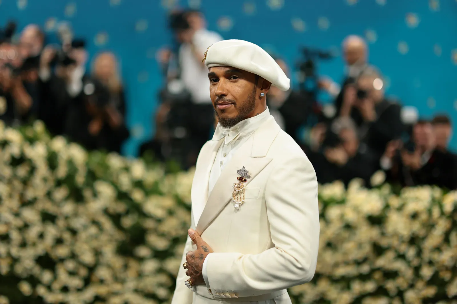 A man in a white beret and white suit poses on the runway.