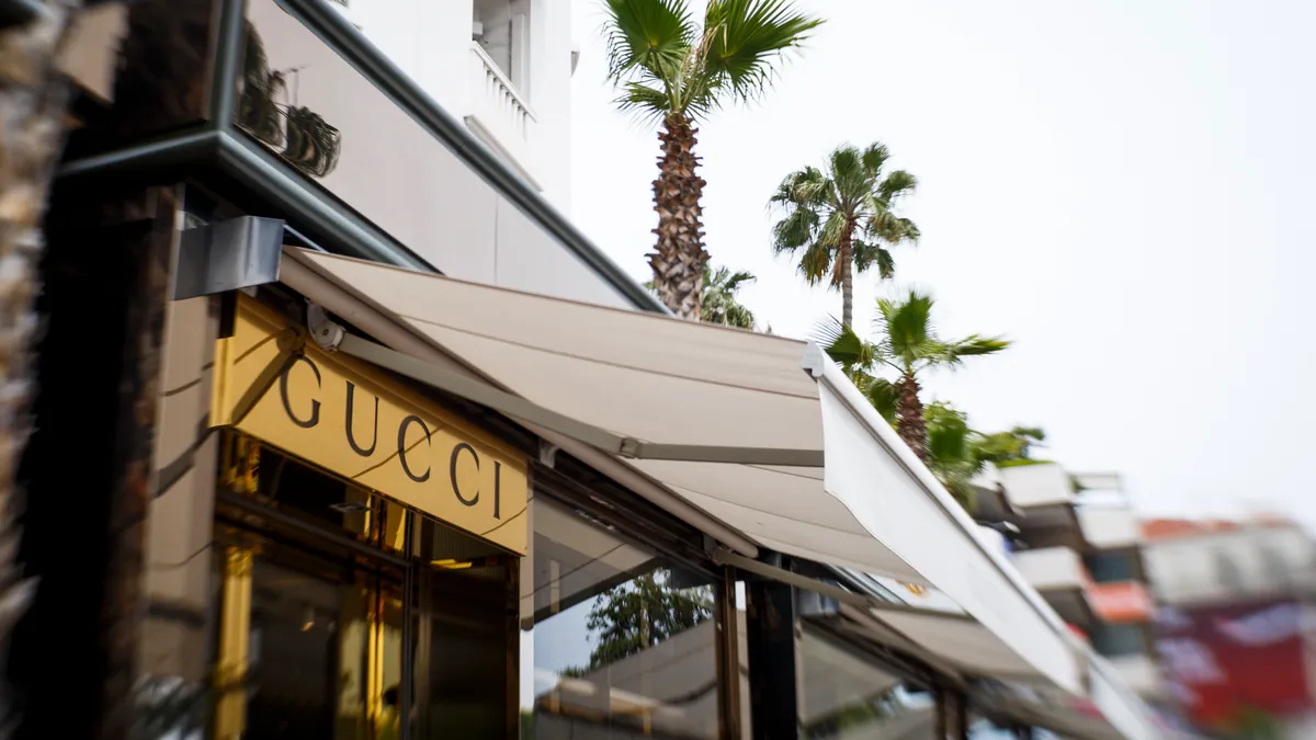 Outside corner view of a Gucci store with gold trim on the facade and palm trees in the background.