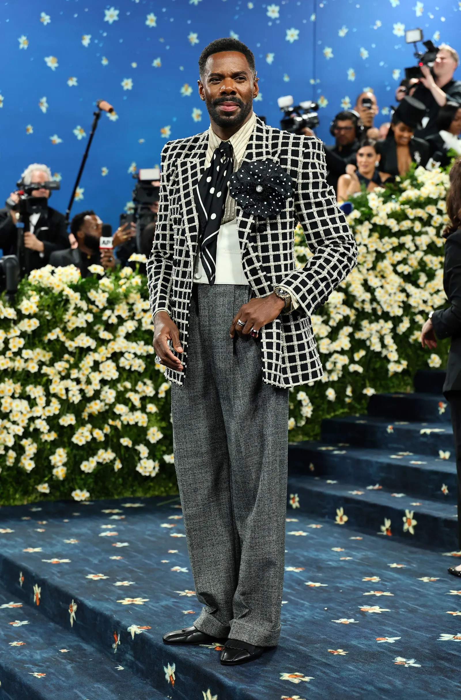 A man in a black and white suit stands on a blue carpet.