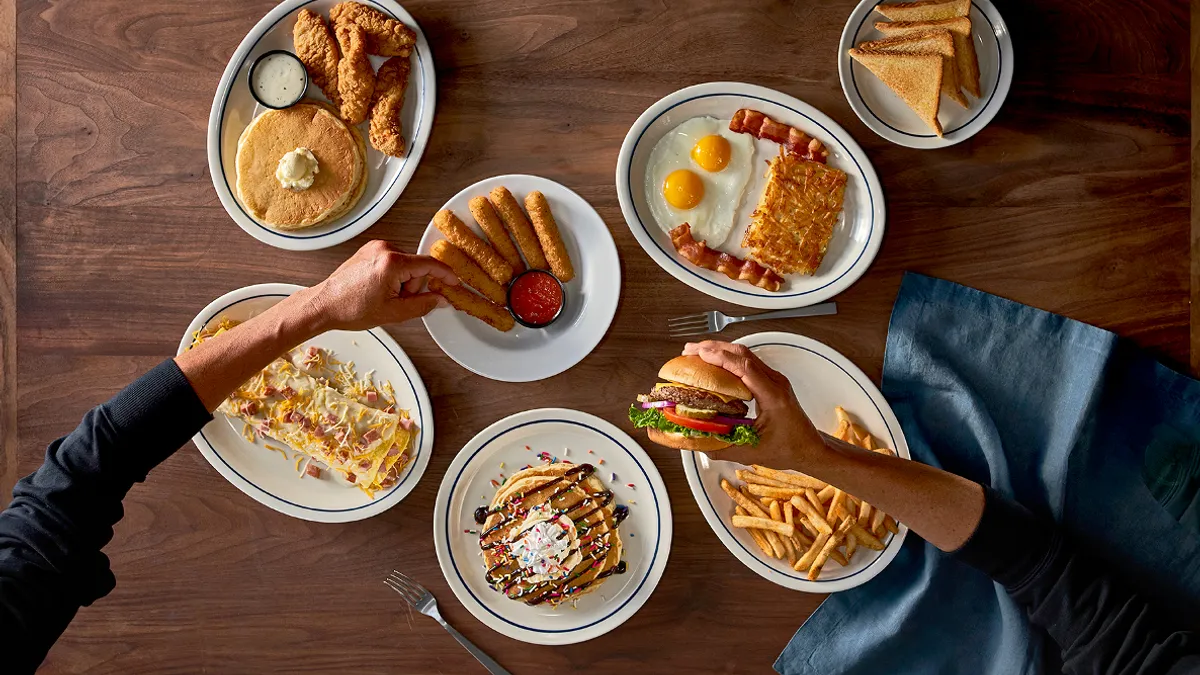 An image of a table and several plates with a burger and breakfast items