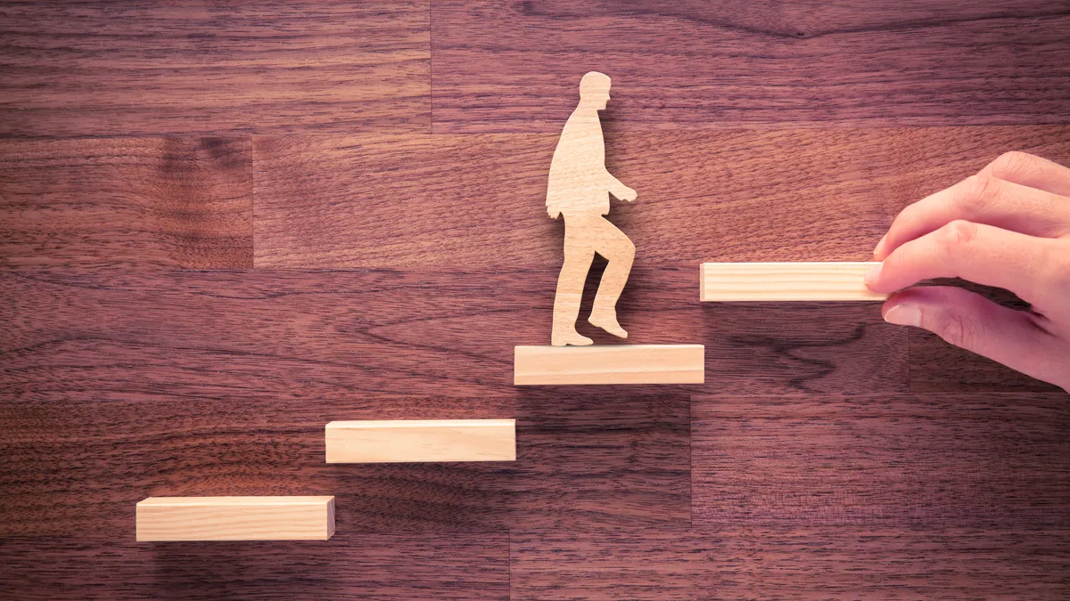 A male wooden figure climbs steps of a ladder.