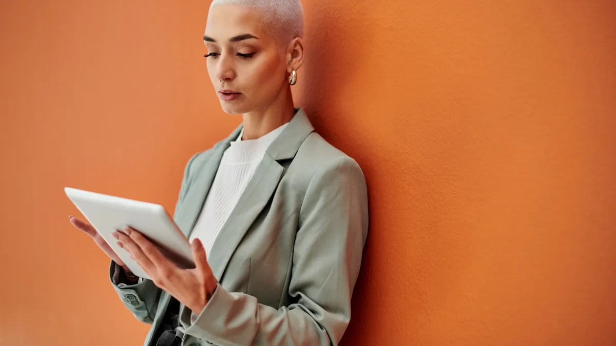 A White person with a shaved head in a blazer types on a tablet