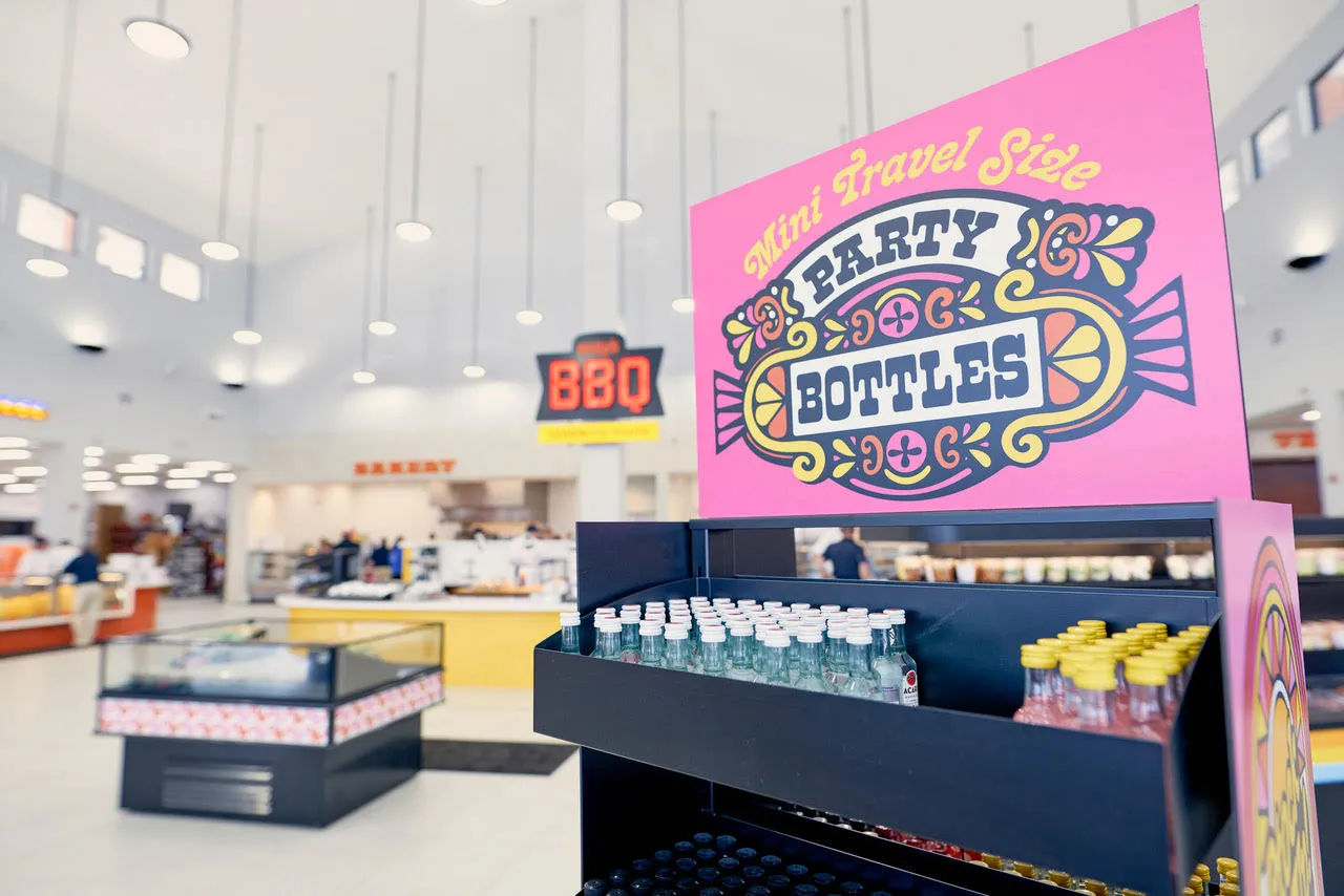 A photo of a display of mini alcohol bottles inside a store. The display says &quot;mini travel size party bottles&quot; and a sign on the wall of the store in the background says &quot;BBQ.&quot;