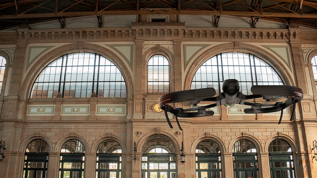 An unmanned, small drone floats in a hall with old gothic architecture-inspired walls.