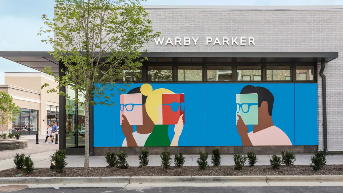 A graphic mural on the side of a Warby Parker depicts three colorful silhouettes of people with eyeglasses against an azure background.