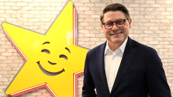 An image of a man wearing a suit in front of a beige brick wall with a giant smiling star in the background.