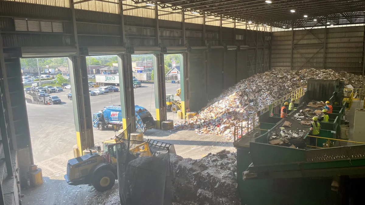 View of recycling facility, with employees sorting material and trucks/heavy equipment