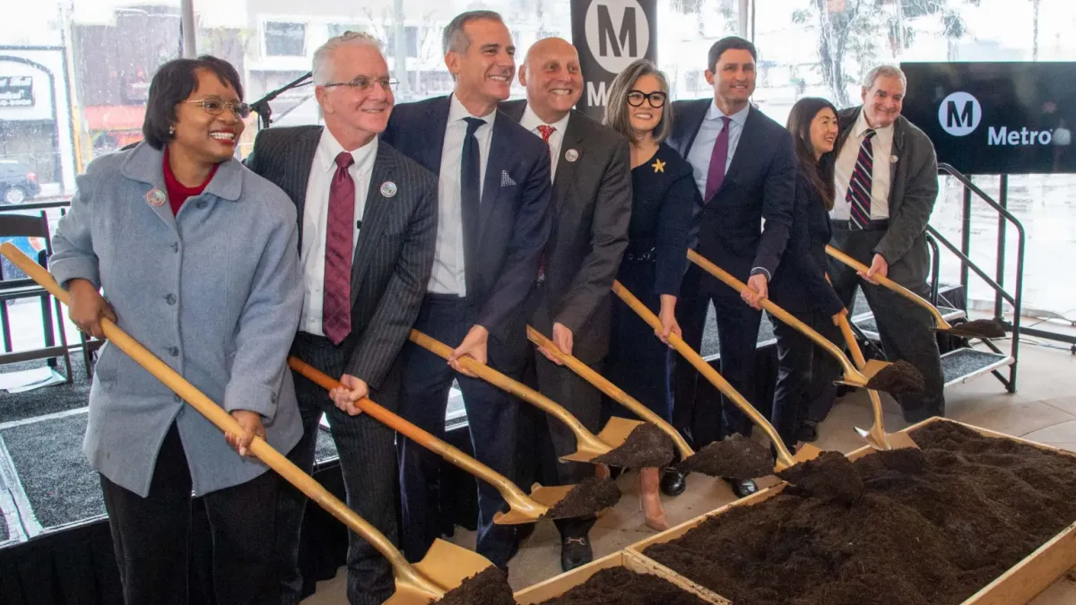 A group of men and women hold shovels.