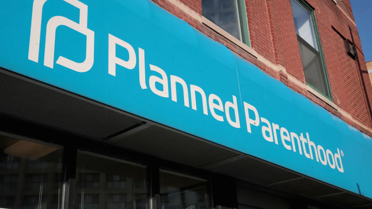 A blue sign that says "Planned Parenthood" hangs above a storefront on a city street.