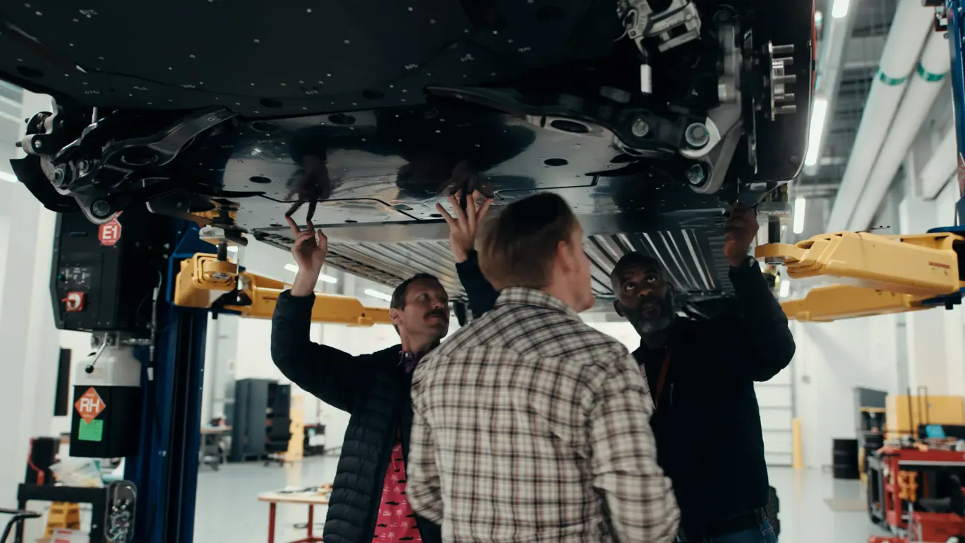 Three Universal EV Platform team members at Ford's Vehicle Performance and Electrification Center working on the underbody shield of a vehicle.