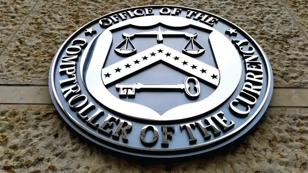 The Office of the Comptroller of the Currency's seal hangs on a brick building.