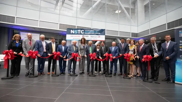 18 people in business attire cutting a red ribbon with bows.