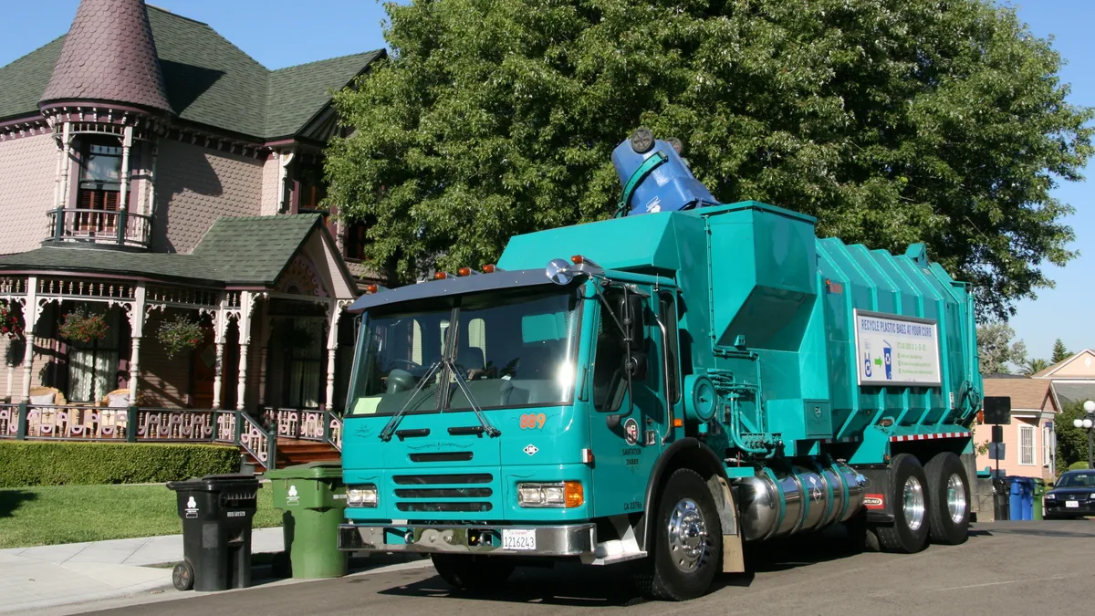 Truck collecting a blue recycling cart in Los Angeles, with a black cart for trash and green cart for organic waste on the curb