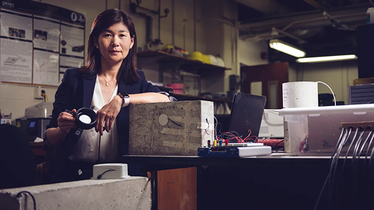 A person poses in a lab area, dimly lit, with a piece of technology.