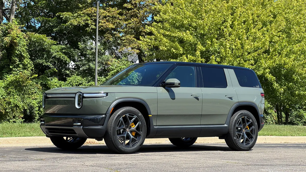 A Rivian R2 crossover SUV sits on gravel, with green trees in the background.