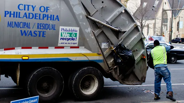 A worker dumps trash into the back of a trash truck