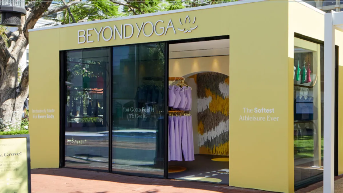 Picture of the outside of a Beyond Yoga pop up shop. Next to the temporary store is a place for four people to sit under a covering.