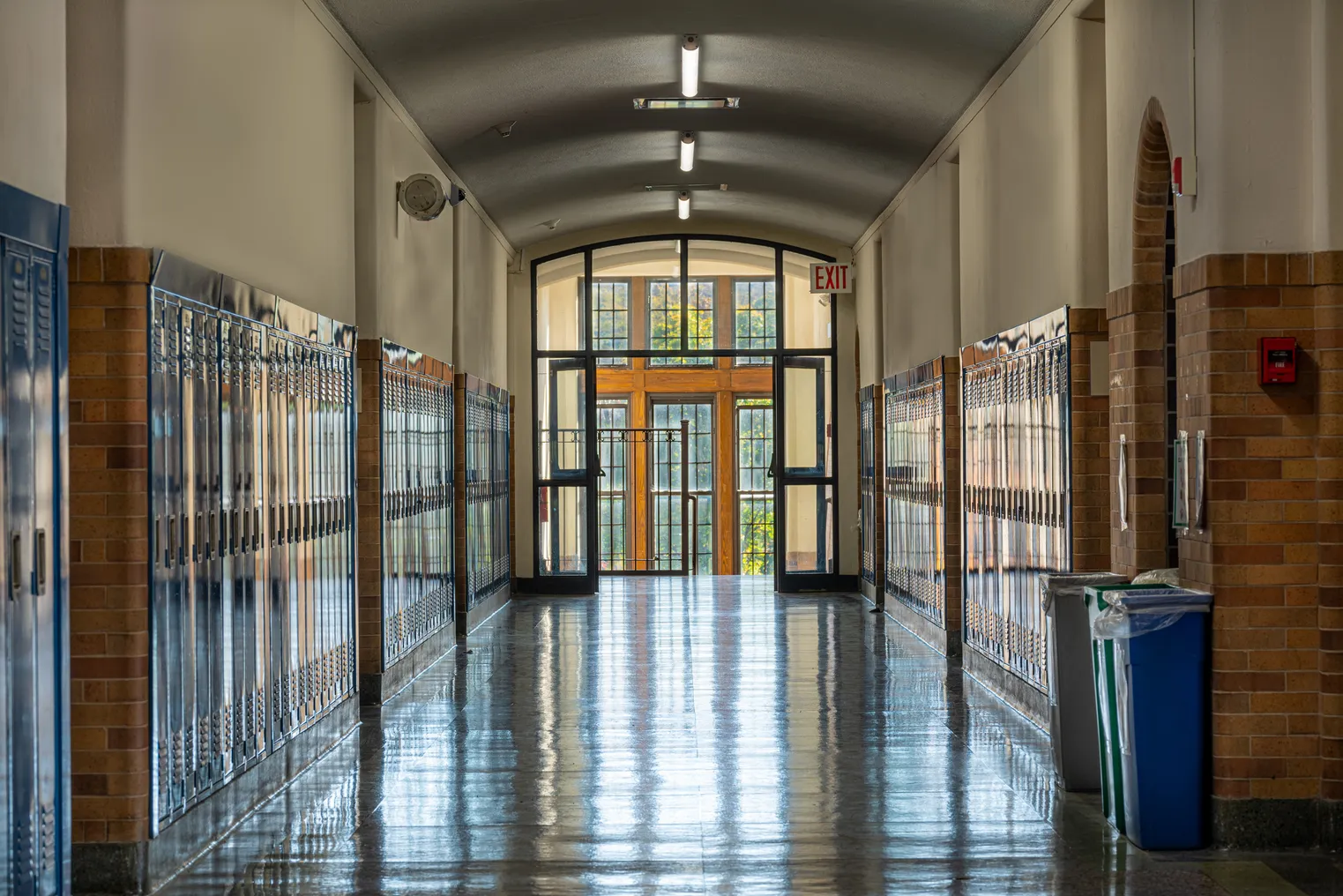 The hallway of a school leads to a stairwell and windows.