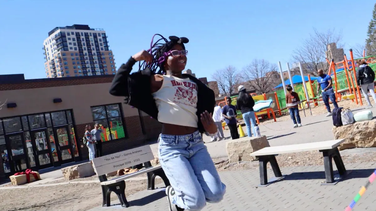 A student is outside on a playground and is jumping up.