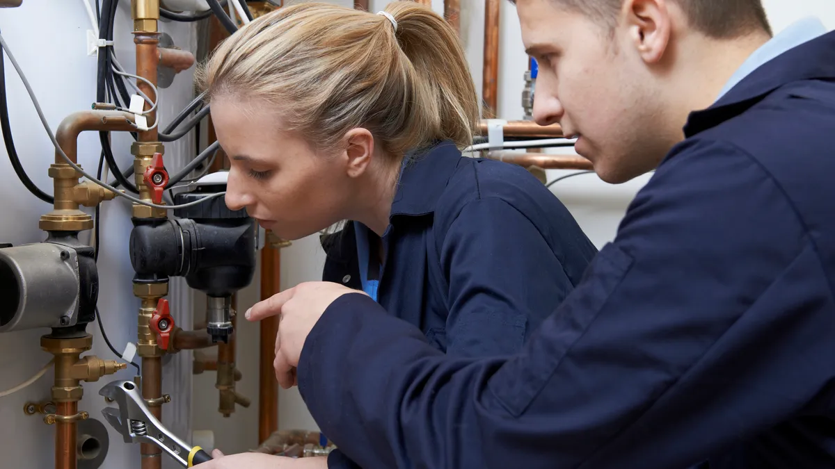 A female trainee plumber is seen working on a central heating boiler.