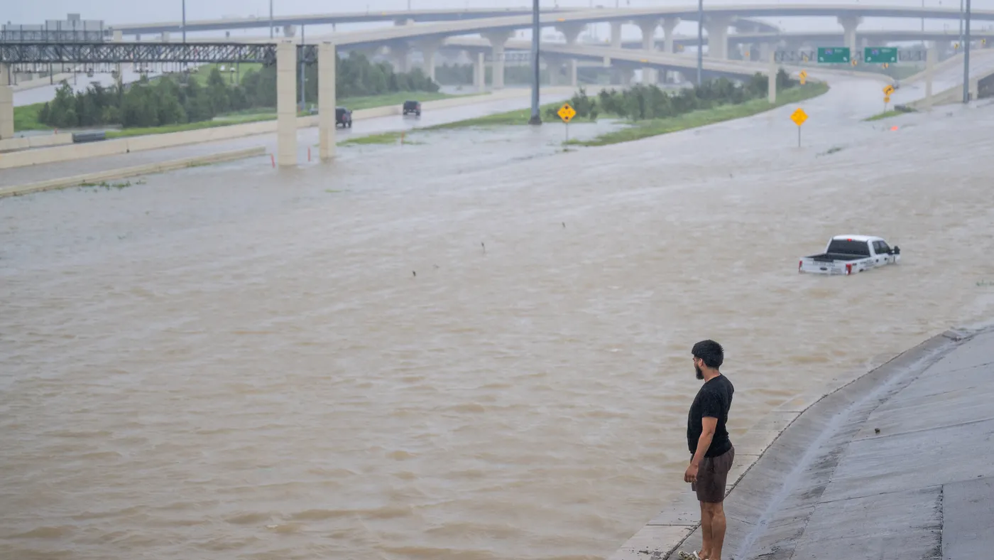 A person looks at a flooded highway with a partly submerged white pickup truck.