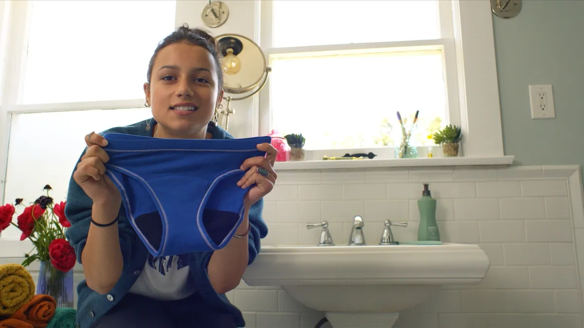 A teenager holds up a pair of blue undies.