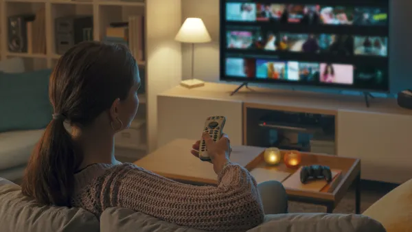 A person holds a remote up while sitting on a living room couch watching TV
