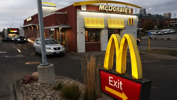 A dawn image of a McDonald's drive-thru. At the foreground is an exit sign and there is a car in the background waiting in line.