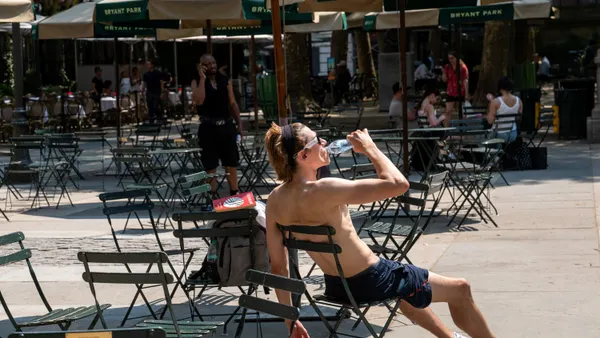 A man sits in a chair drinking water during a heat wave.