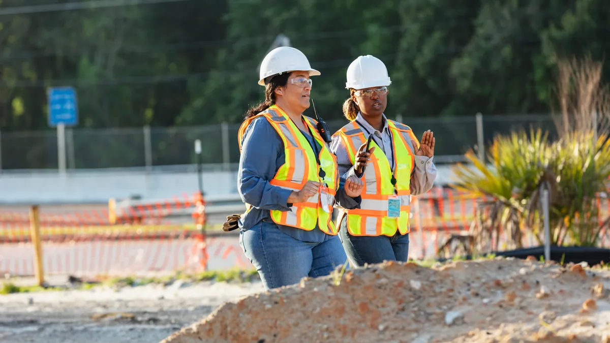 Two women in construction gear walk around dirt mounds on a jobsite.