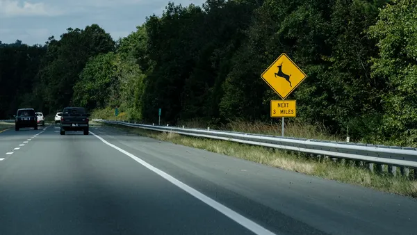 A sign alongside a divided highway warns drivers to be on the lookout for deer crossing the roadway.