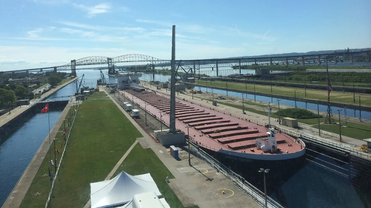 Artificial flat grassy islands stand in channels of water, with a large ship in one and a large bridge in the background.